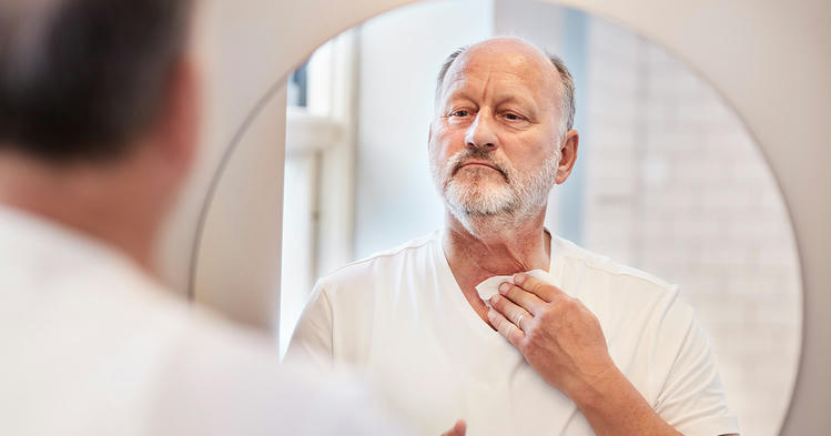 man cleaning his neck stoma in front of mirror